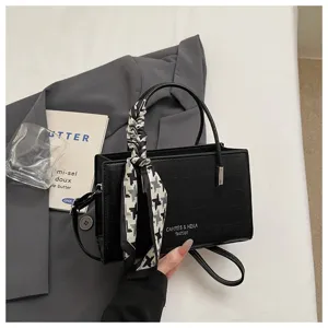 Close-up of black crocodile pattern handbag with stylish houndstooth scarf handle detail.