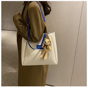 Minimalist white tote bag with blue strap and cute knit bear pendant for women daily commuting.
