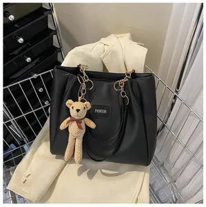 Close-up detail of black tote bag featuring knit bear pendant and metal chain straps.