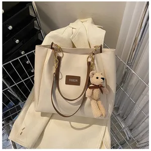 Minimalist beige canvas tote bag with chain strap and cute bear pendant for daily commuting.