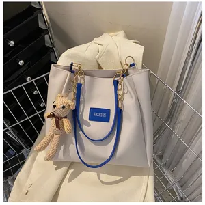 Detail view of casual beige tote bag with blue straps and cute knitted bear pendant.