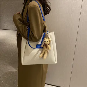 Stylish minimalist white tote bag with blue strap and cute knitted bear pendant for daily commute.