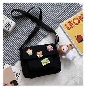 Black canvas crossbody bag with cute badges and plush pendant, casual daily style.