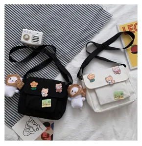 Casual canvas messenger bag with cute cartoon badges and doll pendants for daily use.