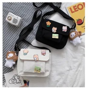 Detailed view of canvas messenger bags in black and white with cute pins and plush charms.