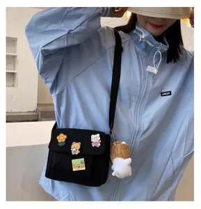 Casual black canvas crossbody bag with cute pins and plush pendant for daily student style.