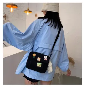 Detail view of cute canvas messenger bag with adorable cartoon pins and plush bear pendant.