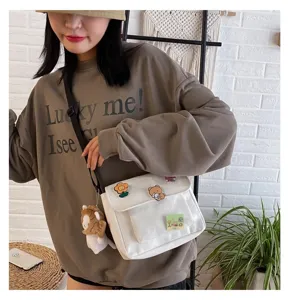 Detailed view of the cute canvas crossbody bag with lovely plush charm and cartoon pins.