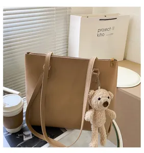 Close-up of stylish beige PU leather tote bag featuring dual shoulder straps and cute bear pendant.