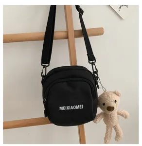 Detailed view of black canvas crossbody bag featuring cute plush bear pendant and front letter print.