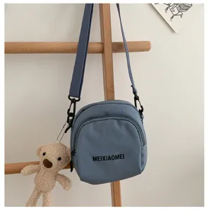 Close-up of a stylish blue canvas crossbody bag with a cute bear charm and adjustable strap.