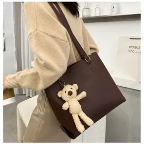 Detail view of brown leather shoulder tote bag with cute bear charm in modern studio.