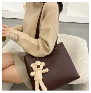 Detail view of brown PU leather tote bag with cute bear pendant, autumn lifestyle shot.
