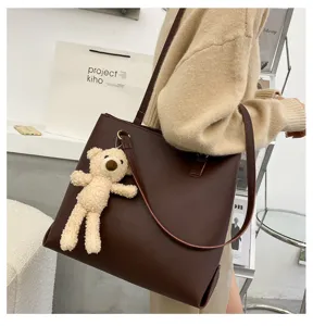 Brown PU leather tote bag detail with cute plush bear pendant in lifestyle setting.