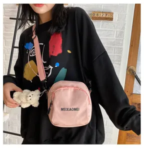 Pink canvas crossbody bag detail shot, featuring a cute small bear plush pendant and zipper.