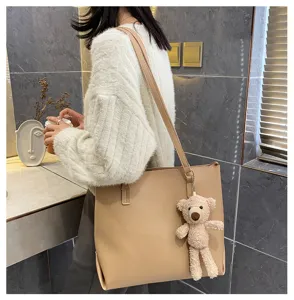 Detail shot of a large beige PU leather shoulder tote bag paired with a cute plush bear charm.
