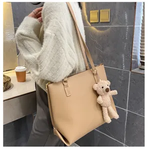 Detail shot of a beige large-capacity shoulder tote bag with a cute bear plush pendant.