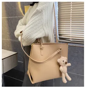 Detail shot of a stylish beige tote bag with a cute plush bear pendant, on-shoulder wear.