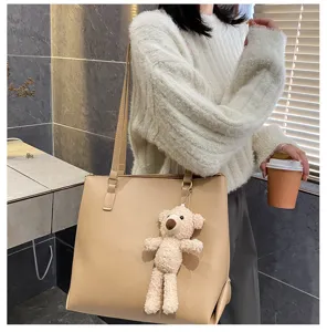 Detail view of khaki leather tote bag featuring cute plush bear pendant, stylish everyday accessory.