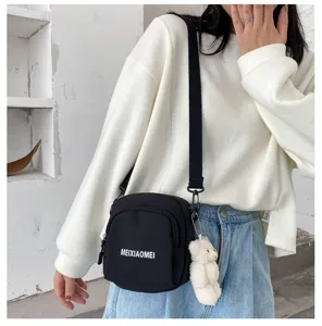 Detail shot of cute black canvas crossbody bag for women with bear pendant and adjustable strap.