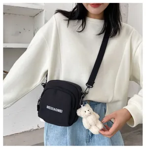 This detailed view features a stylish black canvas crossbody bag with a cute white bear pendant.