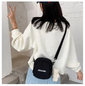 Close-up detail of the black canvas crossbody bag with a cute bear pendant and white text.