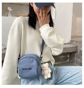 Cute canvas crossbody bag detail showing the adjustable strap and plush bear pendant accessory.