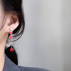 Elegante lange Silberherz-Ohrringe mit funkelnden Steinen und roten Herzanhängern.