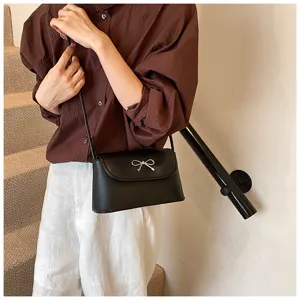 Detail view of stylish black crossbody bag with metal bow accent, trendy underarm design.