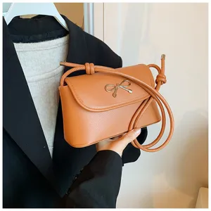 Caramel crossbody shoulder bag detail with elegant metal bow and knotted strap design.