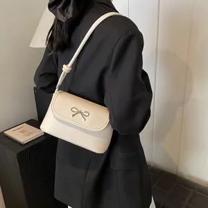 Chic beige shoulder bag for women, elegant baguette style with a cute silver bow detail.
