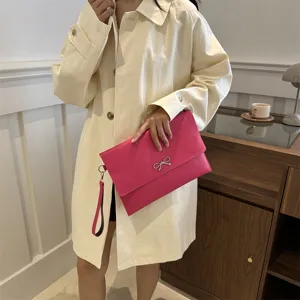 Bolso de mano tipo sobre rosa para mujer con correa de muñeca y lazo de metal.