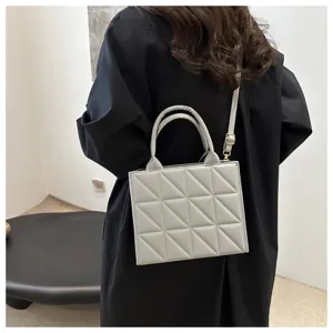 Close-up of stylish light gray quilted structured crossbody bag with top handles detail.