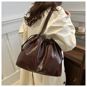 Detail view of a stylish brown PU leather shoulder bucket bag with drawstring and cute bow accent.