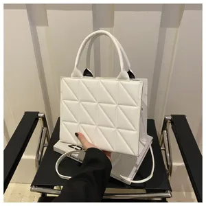 Detailed shot of white quilted geometric handbag with top handles and shoulder strap on display.