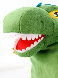 Primo piano di un burattino a mano di dinosauro in peluche verde con denti bianchi.