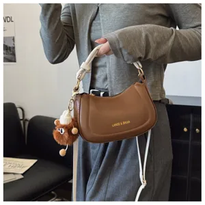 Sac bandoulière croissant minimaliste unicolore avec sangle élégante et pendentif en peluche.
