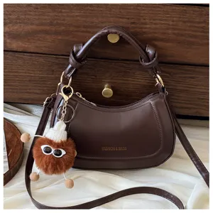 Gros plan sur les détails du sac bandoulière croissant marron foncé avec pendentif pelucheux.