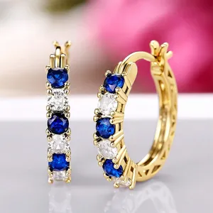 Close-up detail of gold-plated U-shaped hoop earrings with alternating blue and clear zirconia.