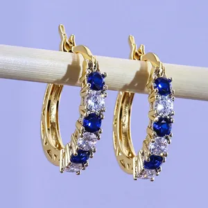 Close-up of gold-plated U-shaped hoop earrings featuring alternating blue and clear cubic zirconia stones.