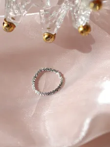 Primo piano di un anello argenteo brillante su raso rosa, trama delicata e splendida luce.