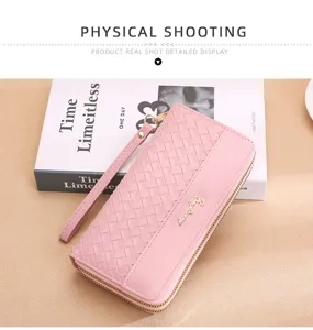 Pink woven long wallet detail view with zipper and wrist strap on beige book prop display