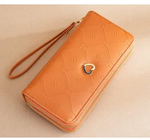 Detailed view of women's orange long double-zipper wallet with chic heart charm and wrist strap.