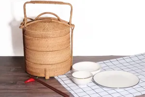 Close-up detail view of handcrafted multi-tier rattan bento box with tableware on table.