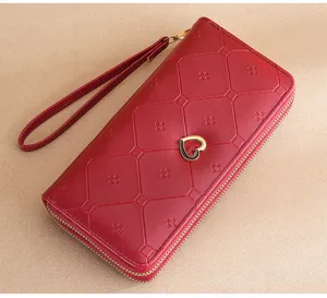 Red leather long wallet detail showing dual zipper, wrist strap and heart metal charm.