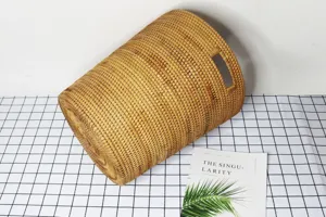 Handmade natural rattan woven laundry basket storage cylinder with side cutout handles.