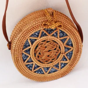 Sac bandoulière rond en rotin tissé avec doublure en tissu floral bleu et lanières en cuir marron.