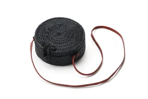 Detailed view of black round woven rattan shoulder bag with adjustable brown leather strap.