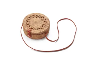 Close-up detail of round woven rattan crossbody bag with brown leather strap and unique pattern.