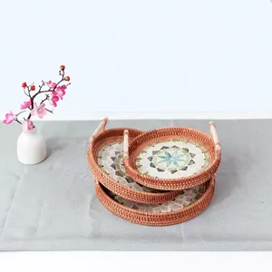 Closeup of round woven rattan tray with wooden handles and beautiful mosaic shell inlay detail.
